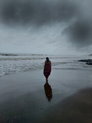 A lady is roaming around on sand at vagator beach in monsoon weather with dark cloud.