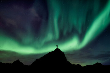 Aurora borealis with starry glowing over hiker standing on summit mountain in the night