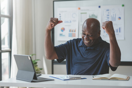 Happy man celebrating success at work with laptop in office setting, smiling and enjoying achievement. Business growth and productivity concept.