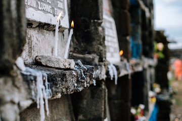 Burning candles in front of the deceased tomb in one of the apartment tombstones during family visit in the cemetery or grave site. Selective focus. Copy space.
