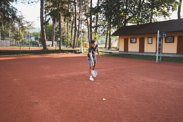 Black-haired athlete with a smile on his face plays badminton on a clay court. Enthusiasm for...