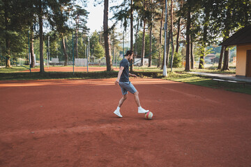 Black-haired athlete plays with a balloon on a clay court. Amateur sport. Individual football training. Soccer. Kicking, striking, passing and dribbling