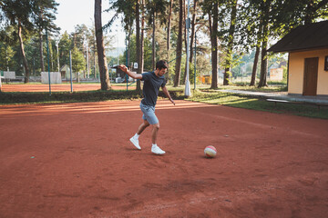 Black-haired athlete plays with a balloon on a clay court. Amateur sport. Individual football training. Soccer. Kicking, striking, passing and dribbling
