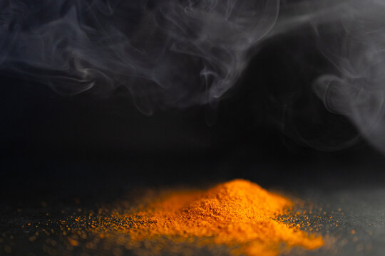 Side view of pile of red parika with smoke around it. Dark background