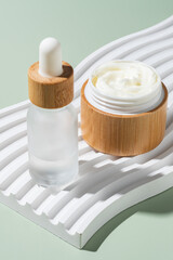 Bamboo cream jar and dropper bottle with face oil on a green background. Cosmetic container mockups. Background for branding and packaging presentation. Natural skincare beauty product concept.
