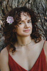 Portrait of beautiful young brunette woman with curly hair smiling in park on sunny summer day
