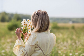 Portrait of a pretty 30+ white woman in a yellow linen dress in a field with a bouquet of field...