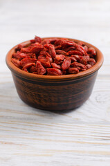 Dried goji berries in a brown ceramic bowl on a white wooden table. Superfood. Vegetarian, vegan. Healthy food concept. Vertical orientation.