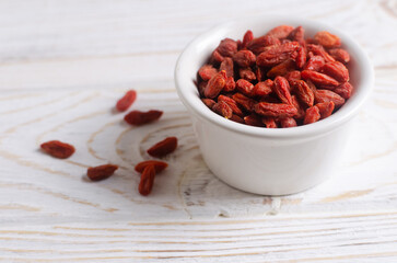 Red dried goji berries in a white ceramic bowl on a light wooden table. Superfood. Vegetarian, vegan. Healthy food concept. Horizontal orientation.