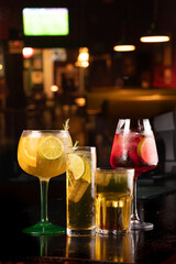 set of drinks of various sizes and refreshing and tropical colors on a dark night background in a blurred Irish bar