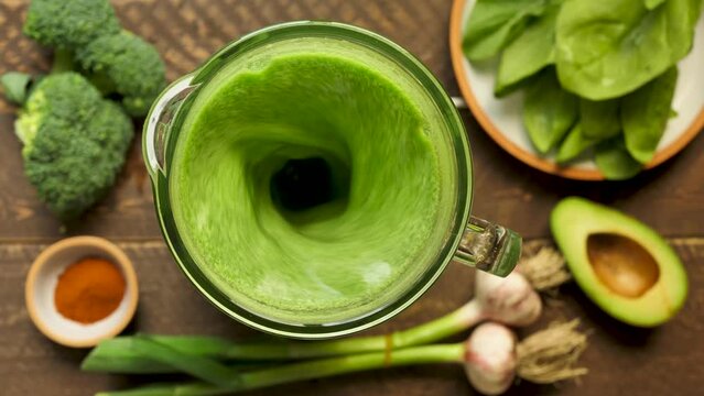Top view mixing green smoothie using a blender. Mix the smoothie in real time in a blender by adding broccoli, garlic, spinach and avocado. Healthy eating and healthy lifestyle. Vegetarian