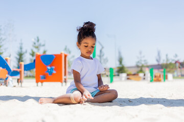 A little mulatto girl plays in the sandbox on the playground