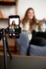 Selective focus on camera of smartphone standing on tripod recording podcast of female blogger or...