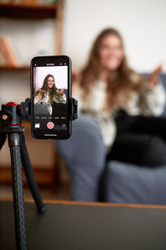 Selective focus on camera of smartphone standing on tripod recording podcast of female blogger or influencer gesticulating and sharing advice with subscribers or followers of her blog or vlog