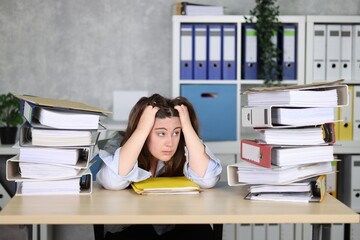 Sekretärin in Bluse, sitzend am Schreibtisch mit verzweifelndem Blick, Hände in den Haaren