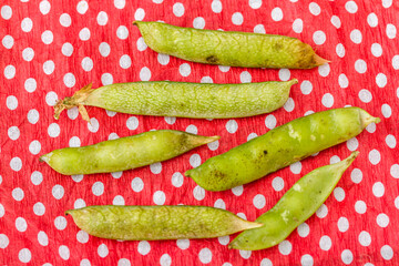 Pea pods, placed on a red and white polka dot fabric background.