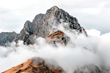 A majestic mountain peak shrouded in a layer of clouds, showcasing rugged terrain and rocky formations amidst an ethereal atmosphere.