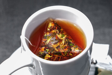 White mug with warm reddish-brown tea with a triangular teabag steeped in hot liquid