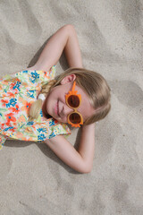 Portrait of cute little girl in floral summer dress laying on the white sand beach.