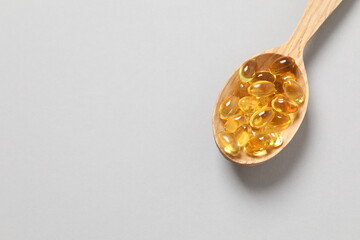 Wooden spoon of Omega-3 capsules on color background with copyspace. Healthcare, wellbeing and supplements.