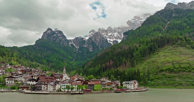 Aerial view of the mountain village of Alleghe in Italy. Beautiful nature landscape of the Dolomite Alps, cityscape with streets and houses on the shore of the lake. High quality 4k footage