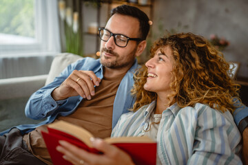 Girlfriend read a book whit boyfriend on sofa at home