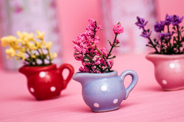 Small polka dot vases in different colors of blue, pink, green and red with colorful flowers on a pink surface and striped background.