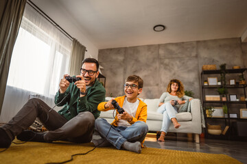 Dad and son play video games with joystick while mum wife watch them