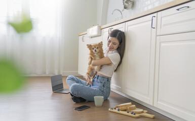 Asian beautiful lady woman work with notebook sit down kitchen floor at home, technology woman concept for alternative office freelance Young happy Asian woman using laptop on lap play with pet dog