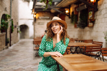 Young woman sitting by table of outdoor sidewalk cafe restaurant, on summer sunny day. People, fashion, lifestyle, travel and vacations