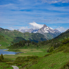 Panorama with a park bench on a hiking trail with a view of a lake and the surrounding mountains in...