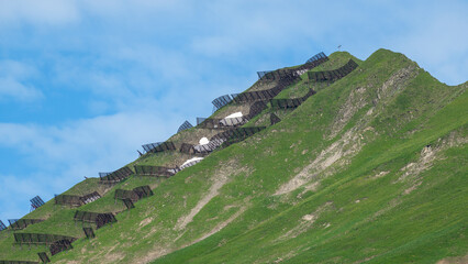 Avalanche barriers on the steep mountain slope above a village in the Bregenzerwald, protection and preservation from masses of snow that destroy everything, iron barriers in spring on the steep slope