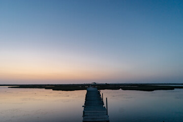 a narrow wooden bridge over a body of water at sunset near the island of Lefkada in Greece