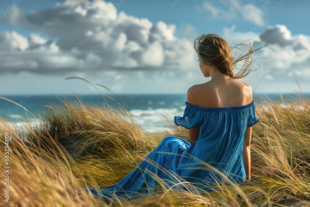 Wall mural A woman sits on the beach wearing a blue dress