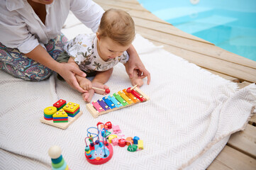Mother and baby playing with colorful educational toys by the pool