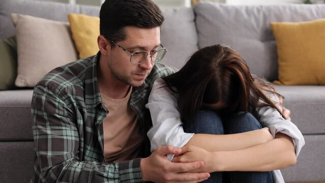 A sympathetic young man provides psychological support to a thoughtful upset loved woman in a difficult life situation, showing loving care, overcoming grief together, or apologizing indoors.