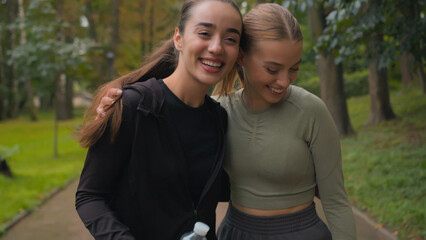 Naklejka premium Two Caucasian happy sporty women girls active sport ladies hugging embrace after fitness training workout outdoors female friends gen z smiling runners walking in park city sports achievement teamwork