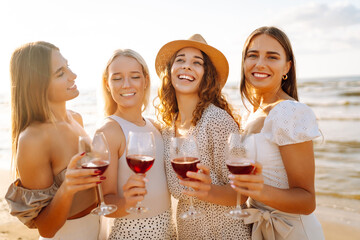 Group of carefree women clinking glasses of wine, smiling cheerfully while having fun and enjoying hen party celebration on coastline. Hen party on the beach.