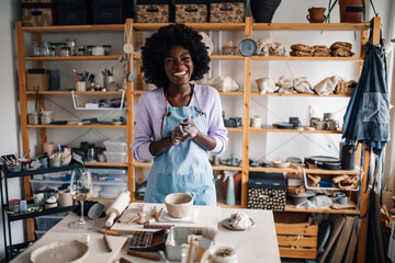 Diverse potter standing at pottery atelier surrounded by clay work.