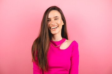 Fototapeta premium Happy cheerful young woman wearing pink long sleeves top rejoicing at positive news or birthday gift, looking at camera with joyful and charming smile. Brunette student girl relaxing isolated pink.