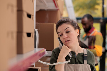 Storage room employee talking at landline phone with remote business owner before start working at...