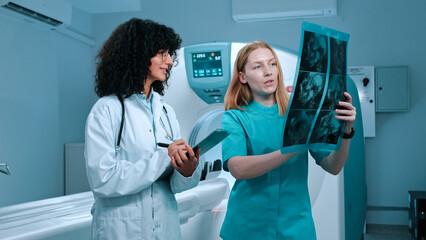 Chef doctor holding MRI scan. Intern with stethoscope holding folder and making notes. Two...