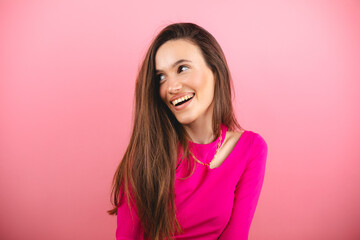 Fototapeta premium Happy cheerful young woman wearing pink long sleeves top rejoicing at positive news or birthday gift, looking at camera with joyful and charming smile. Brunette student girl isolated pink look at side