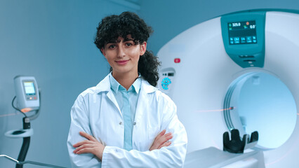 Caucasian tomography specialist posing with crossed arms. Smiling doctor at background of CT...