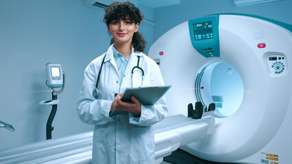 Young tomographer getting ready for procedure. Cheerful doctor smiling at background of MRI...