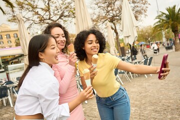 Three young women enjoying ice cream and taking selfies