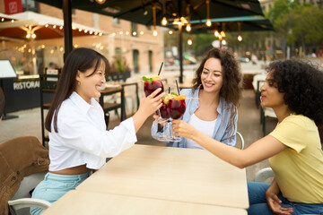 Three young women toasting with drinks at outdoor cafe