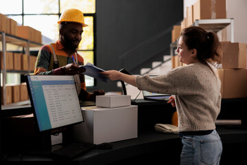 Diverse storage room employee standing at counter desk, discussing merchandise inventory report in warehouse. Stockroom coworkers working at customers orders checking shipping details