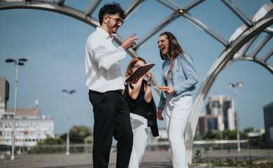Three business colleagues laughing and brainstorming ideas outdoors in an urban setting on a sunny...