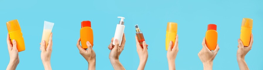 Many hands with bottles of sunscreen cream on light blue background